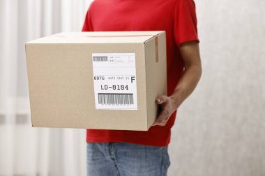 Kapalı mekanda nakliye etiketli paket taşıyan adam, yakın plan. Metin için boşluk