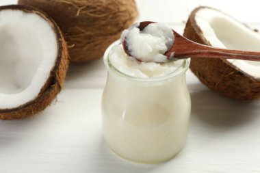 Cam kavanozda organik hindistan cevizi pişirme yağı, kaşık ve beyaz ahşap masada taze meyveler, yakın plan.