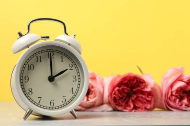 Bahar geldi. Alarm saati ve gri mermer masanın üzerindeki güzel çiçekler sarı arka planda, yakın plan