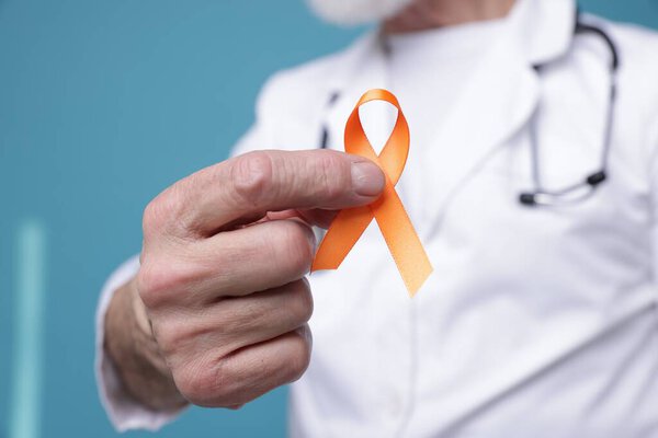 Multiple Sclerosis awareness. Doctor with orange ribbon on light blue background, closeup