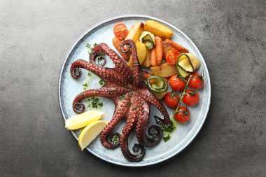 Bitki soslu kızarmış ahtapot, gri desenli masada limon ve sebze.