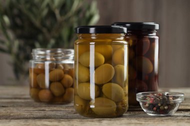 Cam kavanozlarda turşulu zeytin ve ahşap masada baharatlar, yakın plan.
