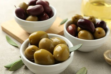 Lezzetli marine edilmiş zeytinler kaselerde ve yeşil yapraklar gri masada, yakın plan.