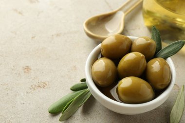 Lezzetli marine edilmiş zeytinler kasede ve yeşil yapraklar gri masada, yakın plan. Metin için boşluk