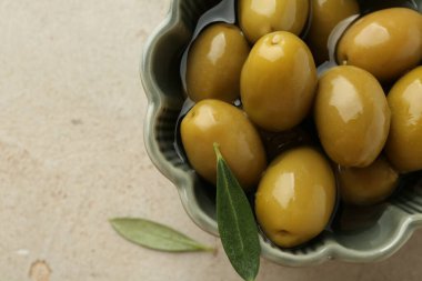 Lezzetli salamura edilmiş zeytinler kasede ve yeşil yapraklar gri masada, üst manzara. Metin için boşluk