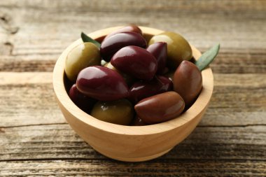 Lezzetli marine edilmiş zeytinler kasede ve ahşap masada yeşil yapraklar, yakın plan.