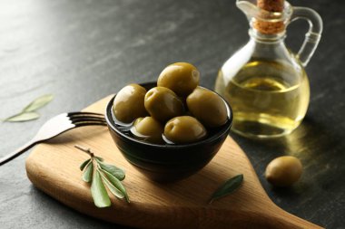 Lezzetli marine edilmiş zeytinler kasede, yeşil yapraklar ve yağ siyah masada, yakın plan.