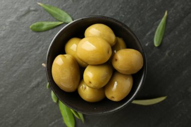 Lezzetli marine edilmiş zeytinler kasede ve yeşil yapraklar siyah masada, düz yerde.