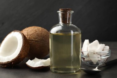 Cam şişede organik hindistan cevizi pişirme yağı, kaşık ve gri masada taze meyveler, yakın plan.