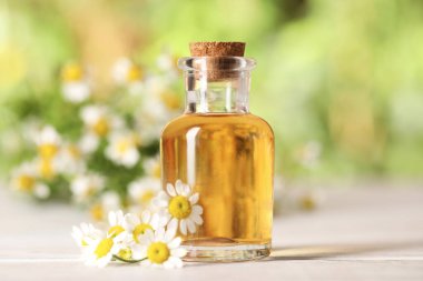 Beyaz ahşap masada, bulanık arka planda, yakın planda, gerekli yağ ve papatya çiçekleri.