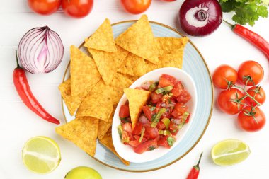 Lezzetli salsa (Pico de gallo) beyaz ahşap masadaki ürünler arasında nachos ile servis edilir.