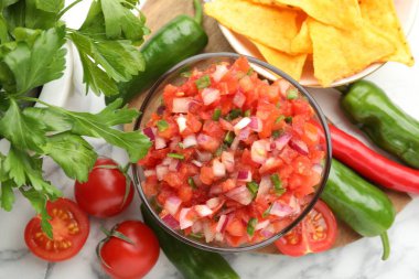 Lezzetli salsa kasesi, nacho cipsi ve beyaz mermer masa üzerindeki malzemeler, düz konum.