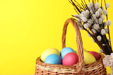 Hasır sepette süslü Paskalya yumurtaları ve sarı arka planda söğüt dalları, yakın plan. Metin için boşluk