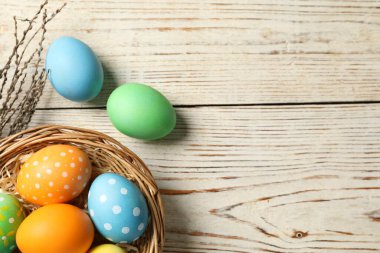 Güzel dekore edilmiş Paskalya yumurtaları, hasır çanak ve söğüt dalları açık ahşap masa, düz uzanmış. Metin için boşluk