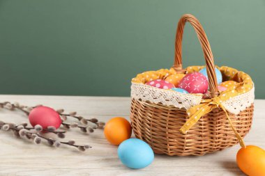 Birçok süslü Paskalya yumurtası hasır sepette ve söğüt dalları ahşap masada yeşil arka planda.