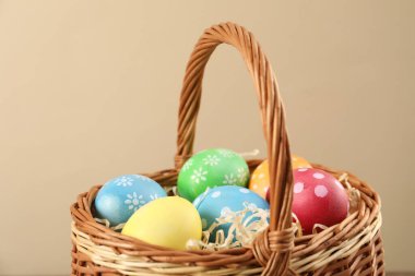 Birçok süslü Paskalya yumurtası bej arka planda hasır sepette, yakın plan