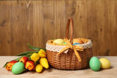 Hasır sepetteki Paskalya yumurtaları ve ahşap masada güzel laleler.