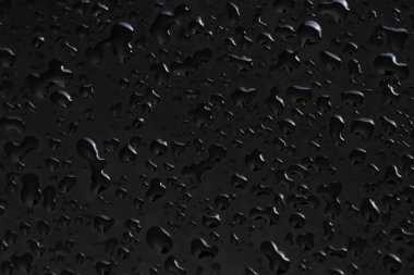 Su siyah cam yüzeyine damlıyor, yakın plan.