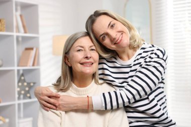 Gülümseyen kızı evde annesine sarılıyor.