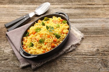 Pişirme kabında sebzeli pilav ve ahşap masada çatal bıçak, metin için yer.