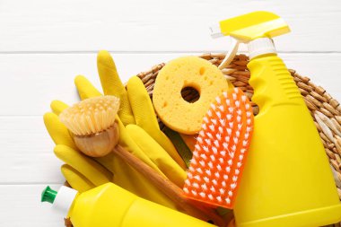 Beyaz ahşap masa üzerinde şişe dolusu temizlik ürünleri ve aletler.