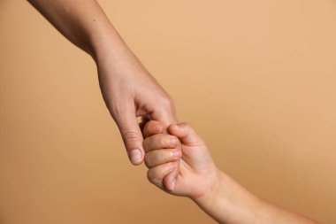 Anne ve çocuk bej arka planda el ele tutuşuyorlar, yakın plan.