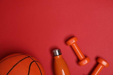 Spor malzemeleri. Dambıllar, su şişesi ve kırmızı arka planda basketbol topu, düz konum. Metin için boşluk