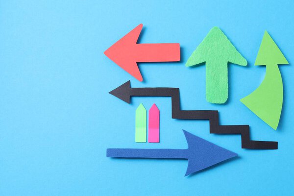 Different paper arrows on light blue background, flat lay