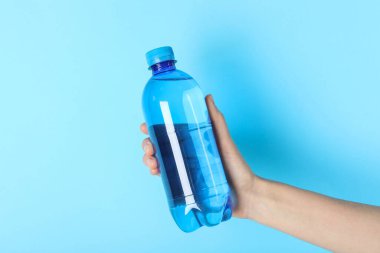 Açık mavi arka planda plastik su şişesi tutan kadın, yakın plan.