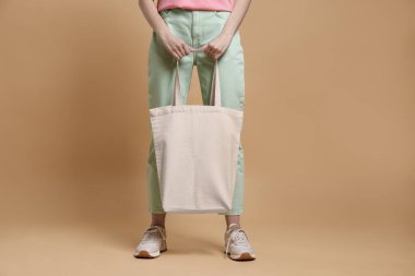 Bej arka planda boş alışveriş torbası olan bir kadın, yakın plan. Tasarım için model