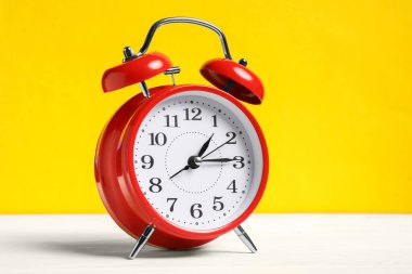 Sarı arka planda beyaz ahşap masada kırmızı bir çalar saat.