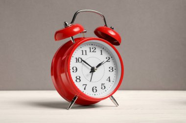 Gri arkaplana karşı beyaz ahşap masa üzerinde bir kırmızı alarm saati