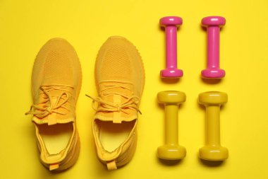 Sarı arka planda dambıllar ve spor ayakkabılar, düz yatış