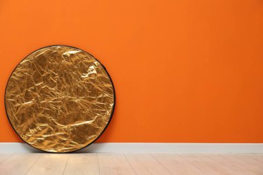 Kapalı alandaki turuncu duvarın yanında bir ışık yansıtıcısı, metin için yer var. Fotoğraf stüdyosu ekipmanı