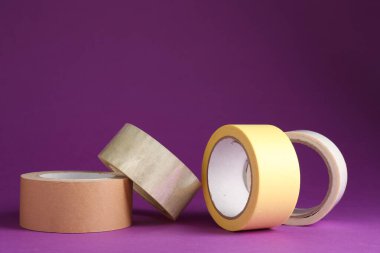 Mor arka planda farklı yapışkan bantların ruloları