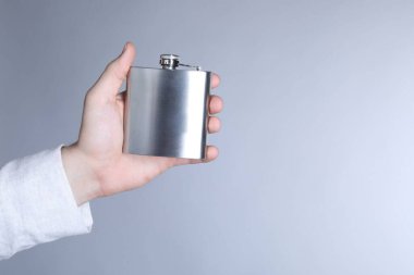 Açık gri arka planda metal bir cep şişesi tutan adam, yakın plan. Metin için boşluk