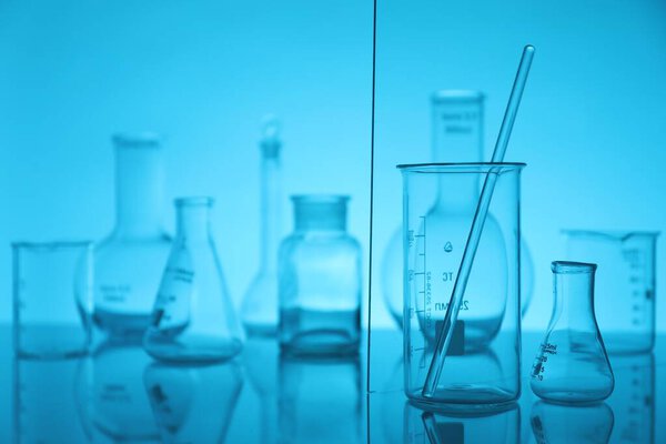 Laboratory glassware on mirror surface against light blue background