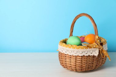 Güzel dekore edilmiş Paskalya yumurtaları hasır sepetin içinde beyaz ahşap masa üzerinde açık mavi arkaplan, metin için boşluk