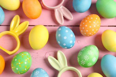 Güzel dekore edilmiş Paskalya yumurtaları ve pembe ahşap masa üzerinde tavşan figürleri.