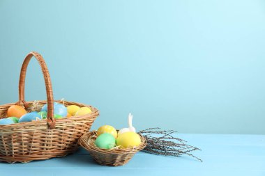 Birçok süslü Paskalya yumurtası hasır sepetlerde ve söğüt dallarında açık mavi ahşap masa üzerinde, metin için boşluk