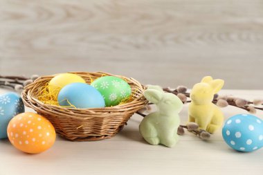 Hasır sepette birçok süslü Paskalya yumurtası, söğüt dalları ve ahşap masada dekoratif tavşanlar, yakın plan.