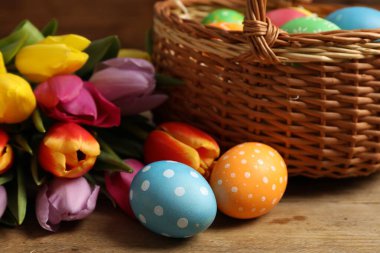 Hasır sepetteki Paskalya yumurtaları ve ahşap masadaki güzel laleler. Yakın plan.