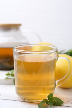 Limonlu aromatik nane çayı ve beyaz ahşap masa üzerinde taze yapraklar, yakın plan.