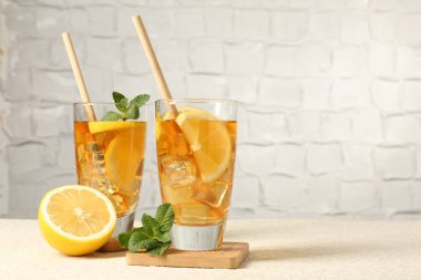 Buzlu çayı pipet, nane ve limon ile tazeleyerek gri arka planda hafif desenli masada, yakın plan. Metin için boşluk