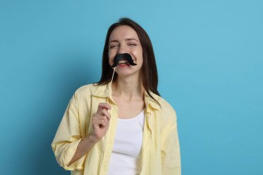 Açık mavi arka planda sahte kağıt bıyıklı mutlu kadın.