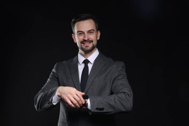 Klasik takım elbiseli yakışıklı adam siyah arkaplanı kontrol ediyor