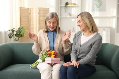 Gülümseyen kız, annesini bir buket lale ve evdeki kanepede hediyeyle tebrik ediyor. Anneler Günün kutlu olsun.