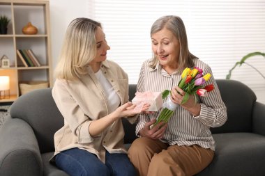 Gülümseyen kız, annesini bir buket lale ve evdeki kanepede hediyeyle tebrik ediyor. Anneler Günün kutlu olsun.