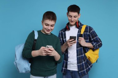 Açık mavi arka planda akıllı telefonları ve sırt çantaları olan öğrenciler