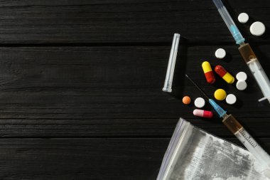 Uyuşturucu bağımlılığı. İçinde toz, şırınga ve haplar olan plastik torba siyah ahşap masada, düz yerde. Metin için boşluk